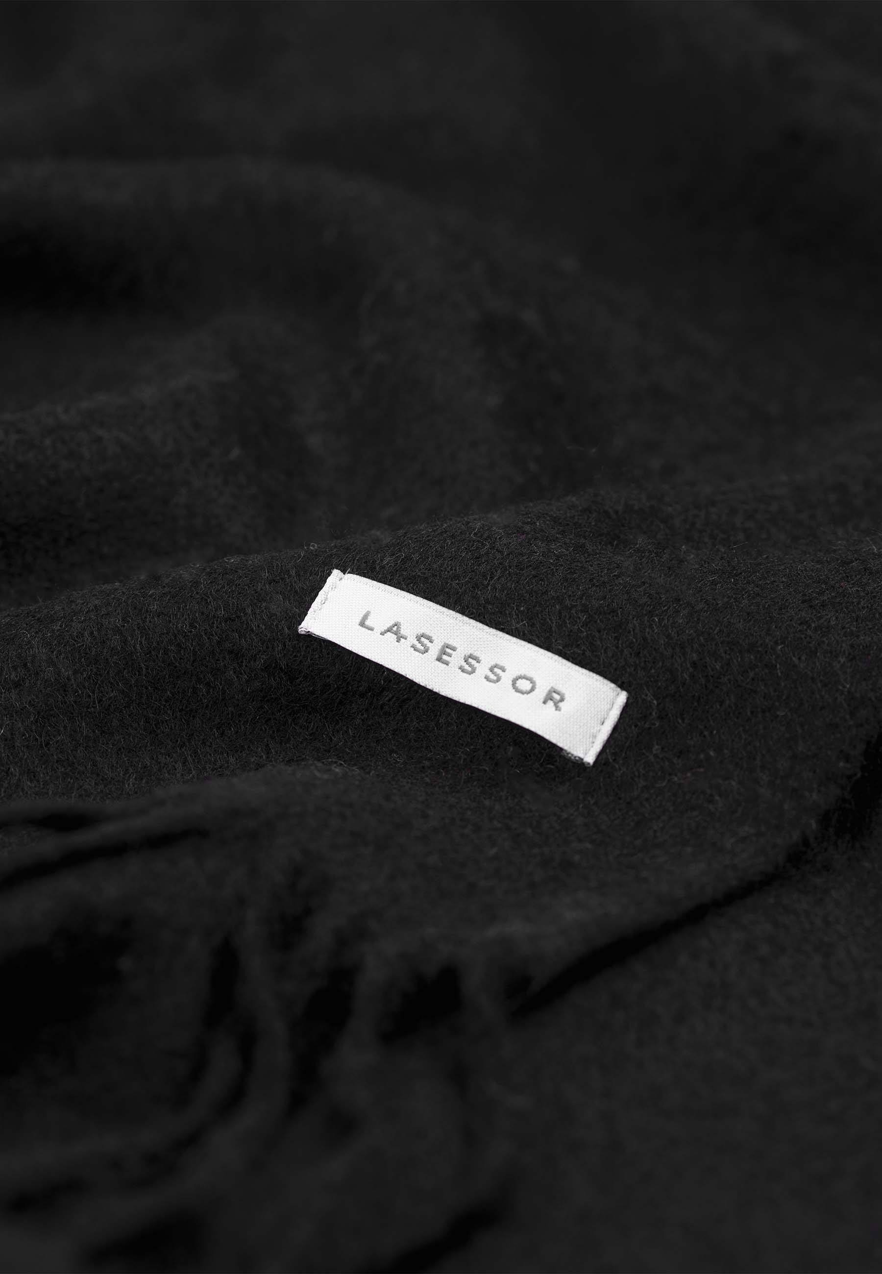 Lähikuva mustasta design villakaulahuivi, jossa Lasessor logo.