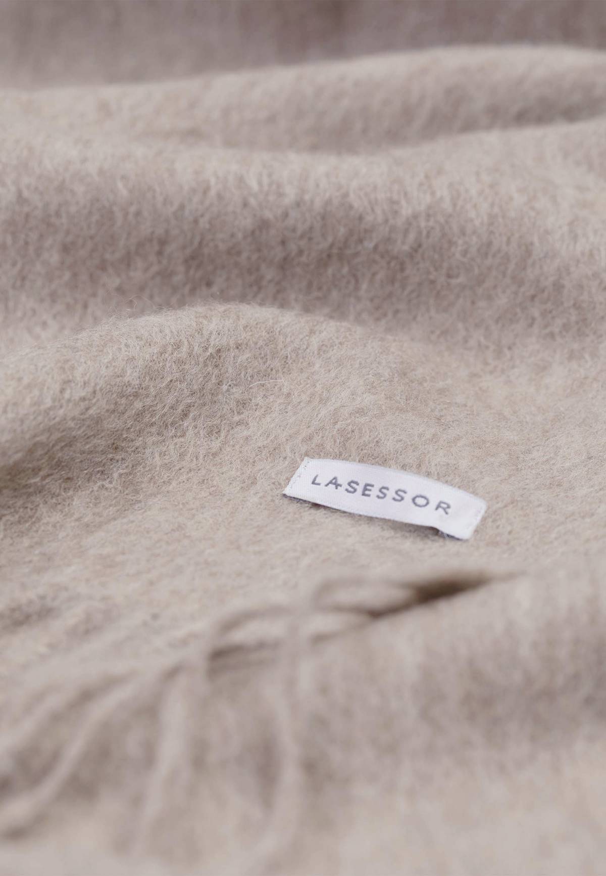 Lähikuva hiekan värisestä Huurteesta, jossa Lasessor logo. Villakaulahuivi.