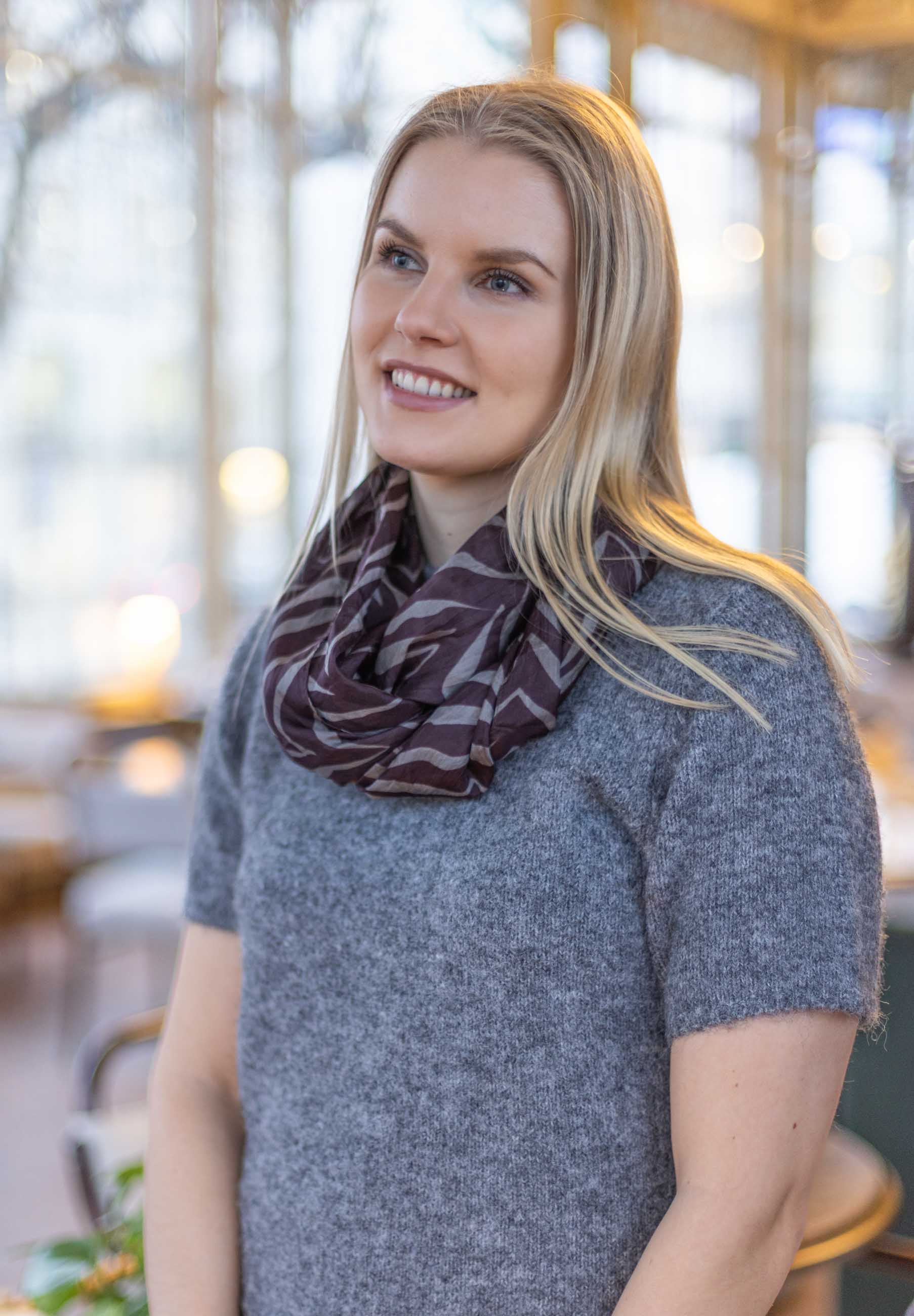 Naissella käytössä viininpunainen kauniisti laskeutuva Belen tuubihuivi arkiasussa neuleen kanssa