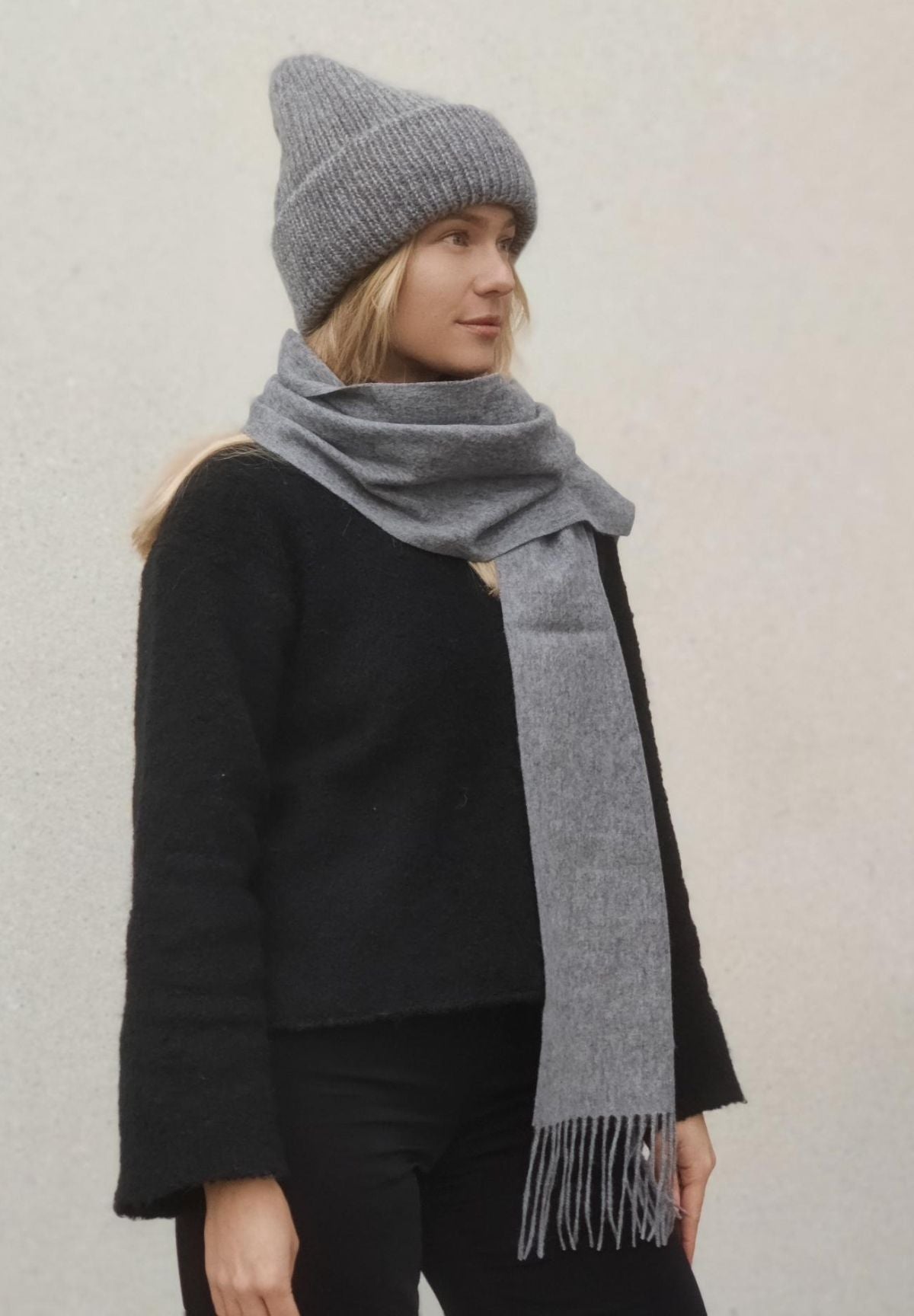 Kuvassa malli, jolla on mustat vaatteet, harmaa Huurre villakaulahuivi ja Mollie pipo.
